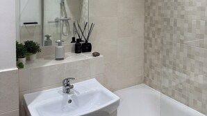 Ein modernes Badezimmer mit einem weißen Waschbecken, einem Spiegel und einer Dusche.