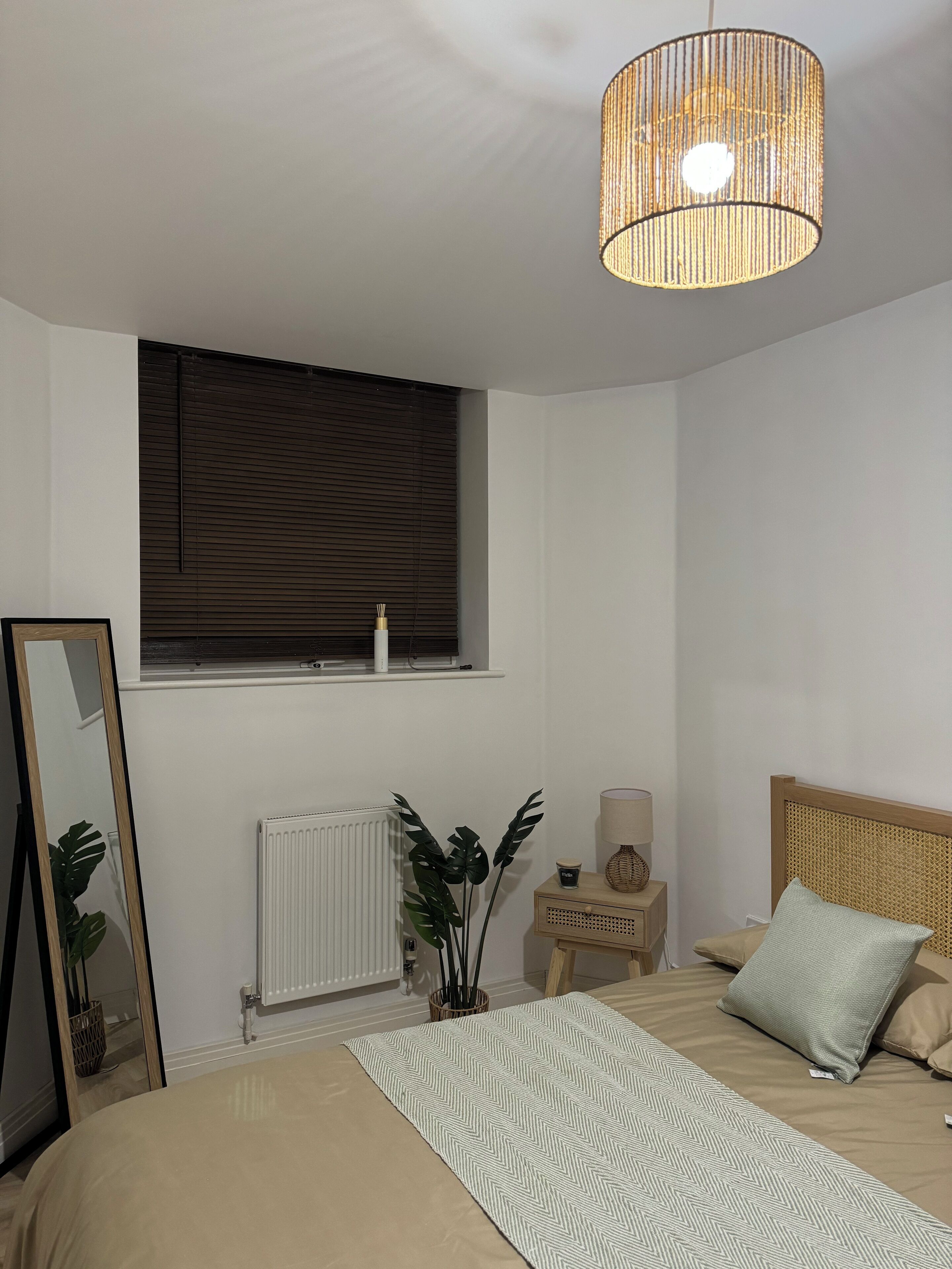 Ein Schlafzimmer mit Bett, Nachttisch, Lampe, Fenster, Heizkörper und einer Pendelleuchte.
