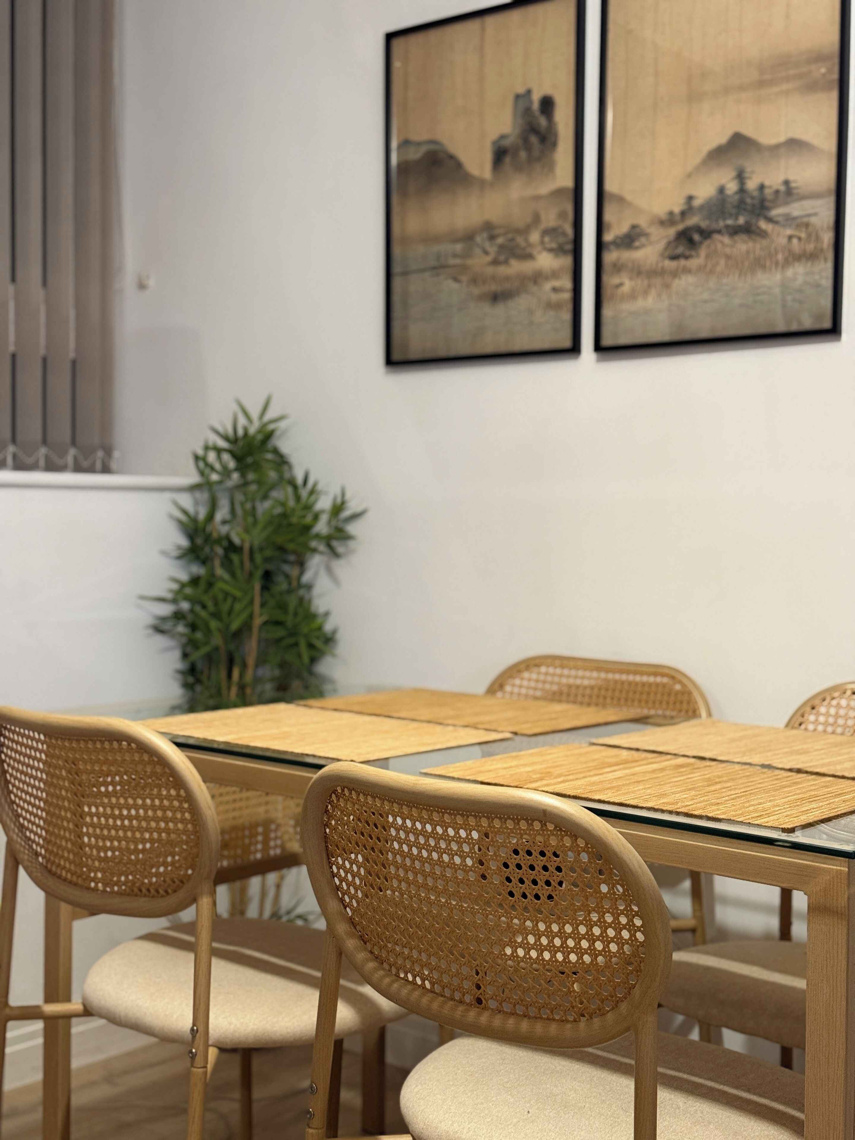 A dining area with a wooden table and chairs, a potted plant, and two framed artworks on the wall.