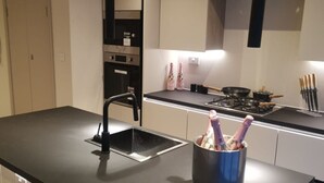 A modern kitchen with a black countertop, stainless steel appliances, and a hanging light.