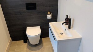 A modern bathroom with a white toilet, a sink with a black faucet, and a dark wall.