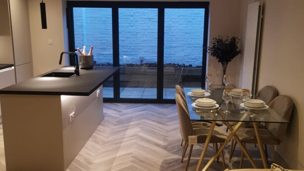 A modern kitchen with a large island, a dining area with a glass table and chairs, and a view of the sea through large windows.