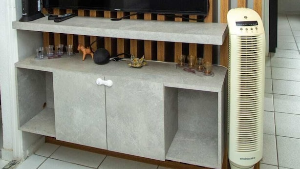 Un salon moderne avec un téléviseur à écran plat fixé sur un mur composé de lattes de bois, un meuble de rangement intégré en dessous et un climatiseur vertical placé à droite.