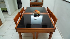 Une table à manger avec un plateau en verre et des chaises en bois, dans une pièce aux murs blancs et au sol carrelé.