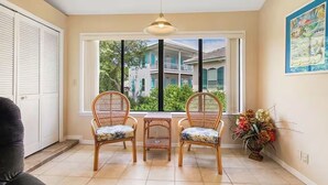 A room with a window view of a house, two wicker chairs, a small table, and a vase with flowers. - Chateau La Mer II #804- Blue Ocean Getaway (Destin)