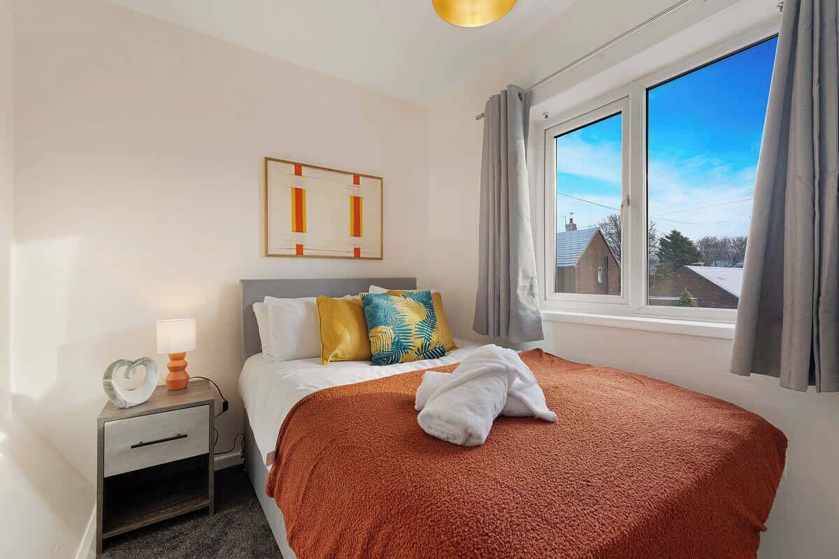 Habitación de hotel con cama, mesita de noche con lámpara, ventana con cortinas y vistas al exterior.