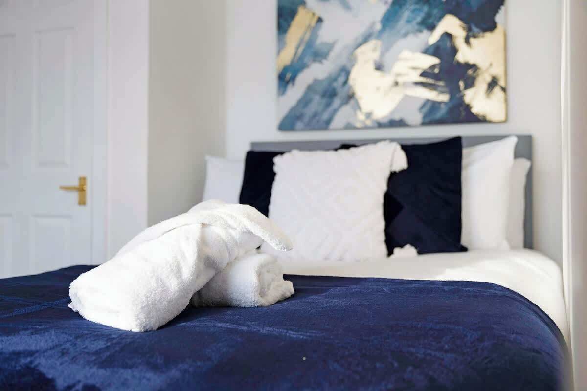 Una cama bien hecha con una toalla blanca y una colcha azul oscuro en una habitación de hotel.
