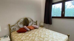 A neatly made bed with a patterned bedspread, a bedside table with a lamp, and a window with curtains. - Villa among olive trees with garden and parking • Relax in Puglia (Puglia)