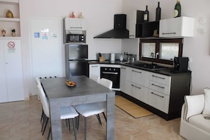 Een kleine keuken met een eettafel, stoelen, een fornuis, oven, magnetron en een spoelbak.