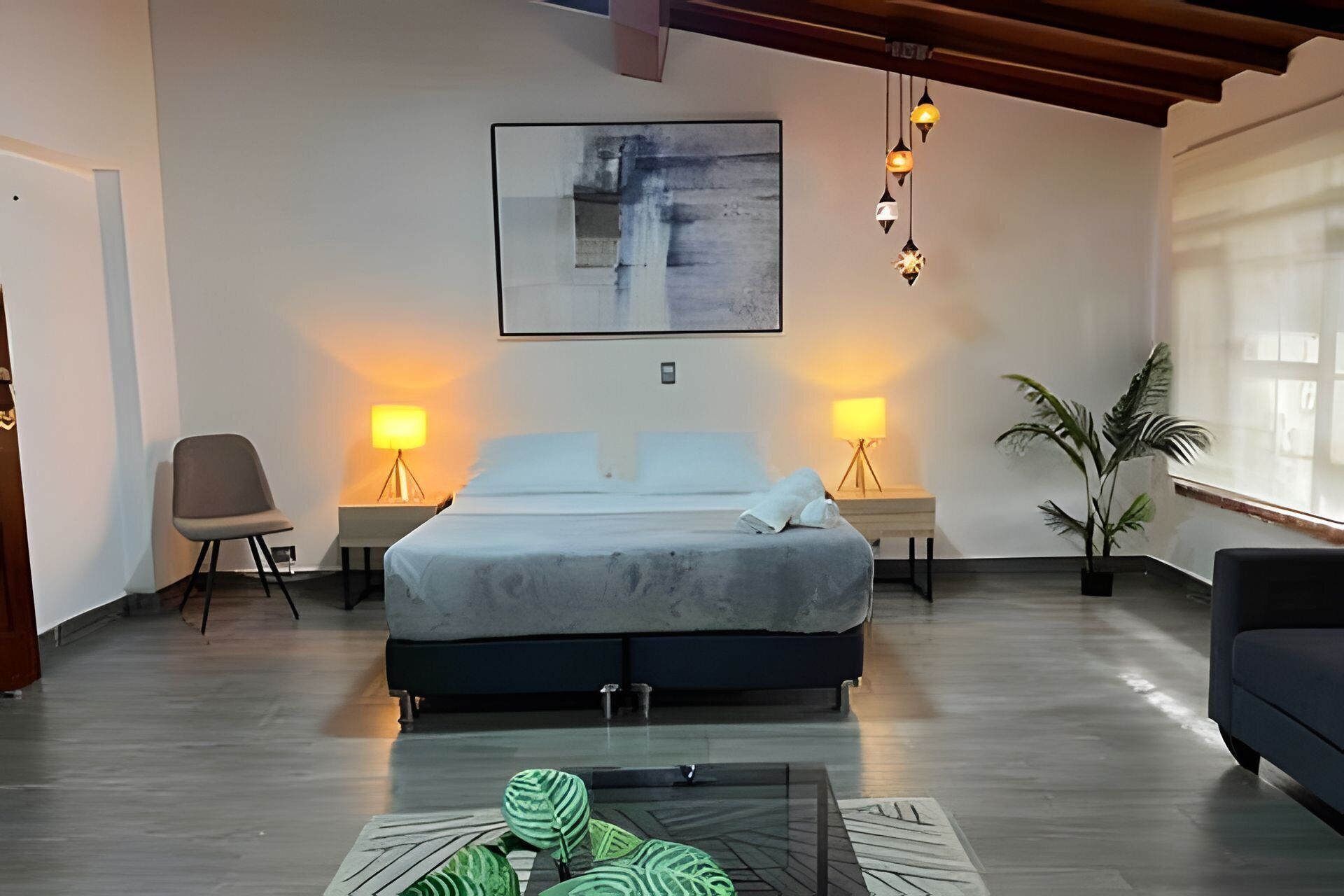 A modern bedroom with a large bed, two bedside lamps, a chair, and a potted plant.