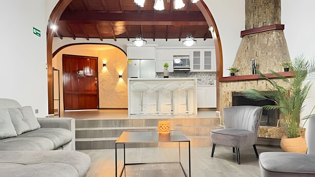 A modern living room with a fireplace, a kitchen in the background, and a wooden ceiling. - Apto Palos Altos  (Medellin)