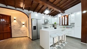 A modern kitchen with white cabinetry, a central island with bar stools, a stainless steel refrigerator, and a stone accent wall. - Apto Palos Altos  (Medellin)
