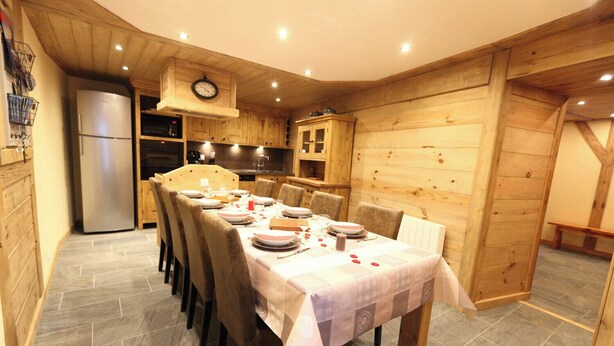 Ein Essbereich mit einem langen Tisch, der für eine Mahlzeit gedeckt ist, Holzwänden und einer Küche im Hintergrund.