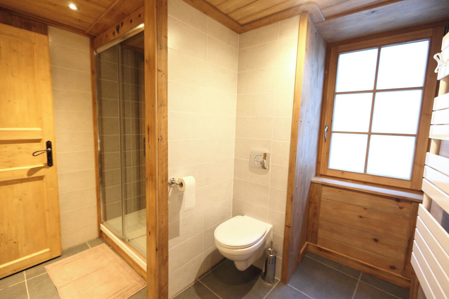 A compact bathroom with a shower, toilet, and wooden cabinetry.