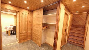 Ein Zimmer mit Holzwänden und Fliesenboden, das eine Essecke mit Tisch und Stühlen, einen Kleiderschrank mit Ablagefläche sowie eine Treppe bietet.