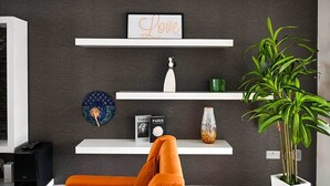 Un soggiorno moderno con una parete scura, mensole bianche, un'insegna con la scritta 'Love', un piatto decorativo, un vaso, un libro intitolato 'PARIS' e una pianta in vaso.