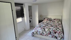 Un dormitorio con una cama, lavadora y puerta que da a otra habitación.