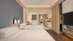 Habitación de hotel con dos camas, televisión, escritorio y baño visible a través de una puerta abierta.