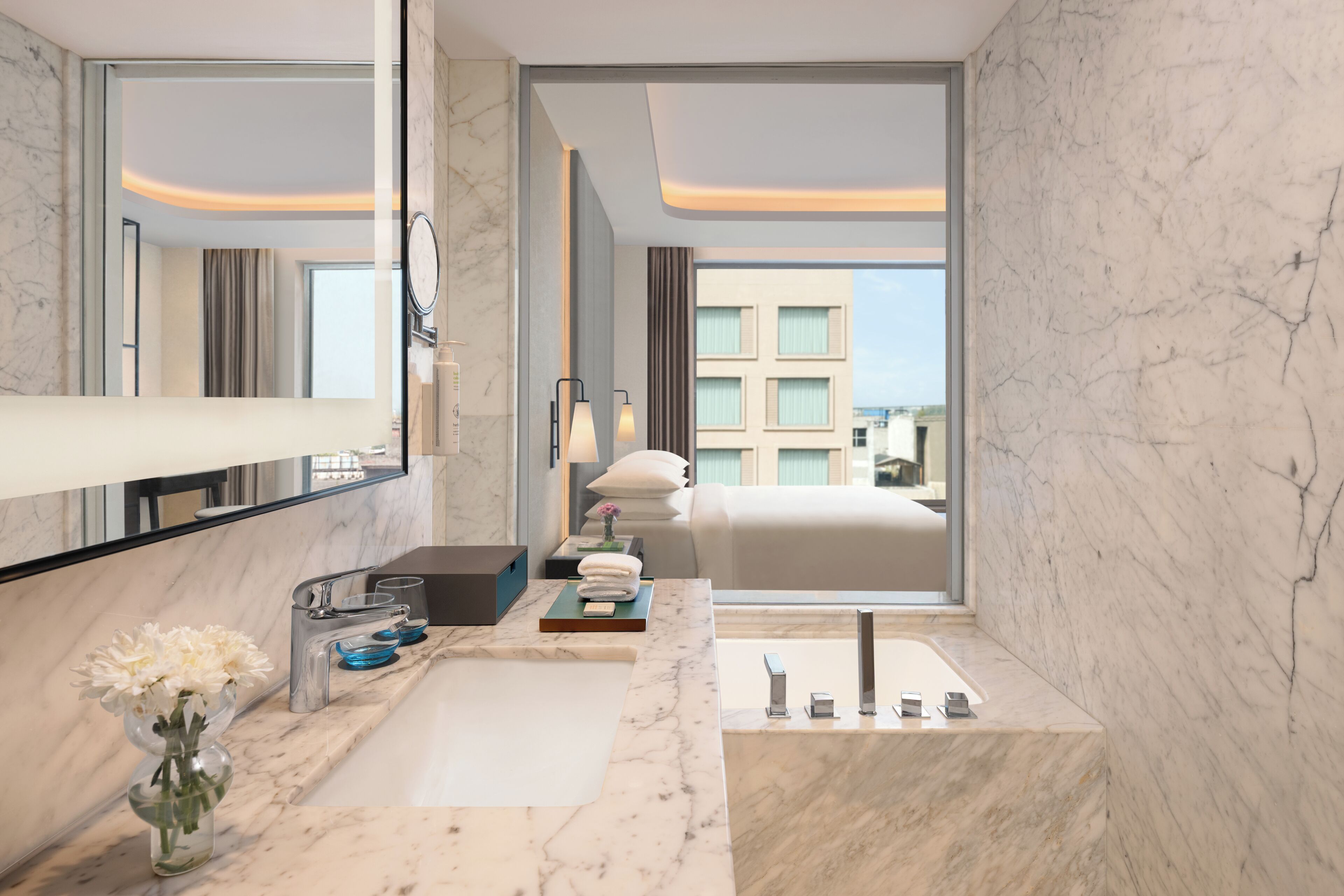 A modern bathroom with a marble countertop, a large mirror, and a view of a building outside.