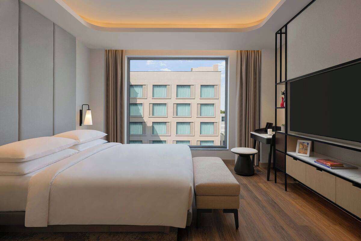 Een moderne hotelkamer met een groot bed, een bureau, een flatscreen-tv en een raam met uitzicht op een gebouw.