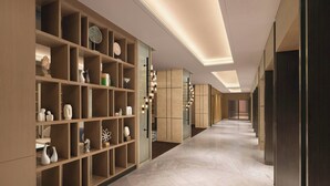 Un corredor moderno de hotel con suelo de mármol, estanterías de madera e iluminación empotrada.