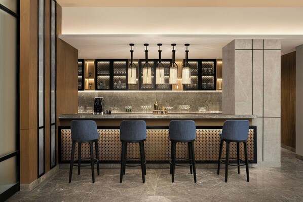 Zona de bar moderna con encimera de mármol, cuatro taburetes y lámparas colgantes.