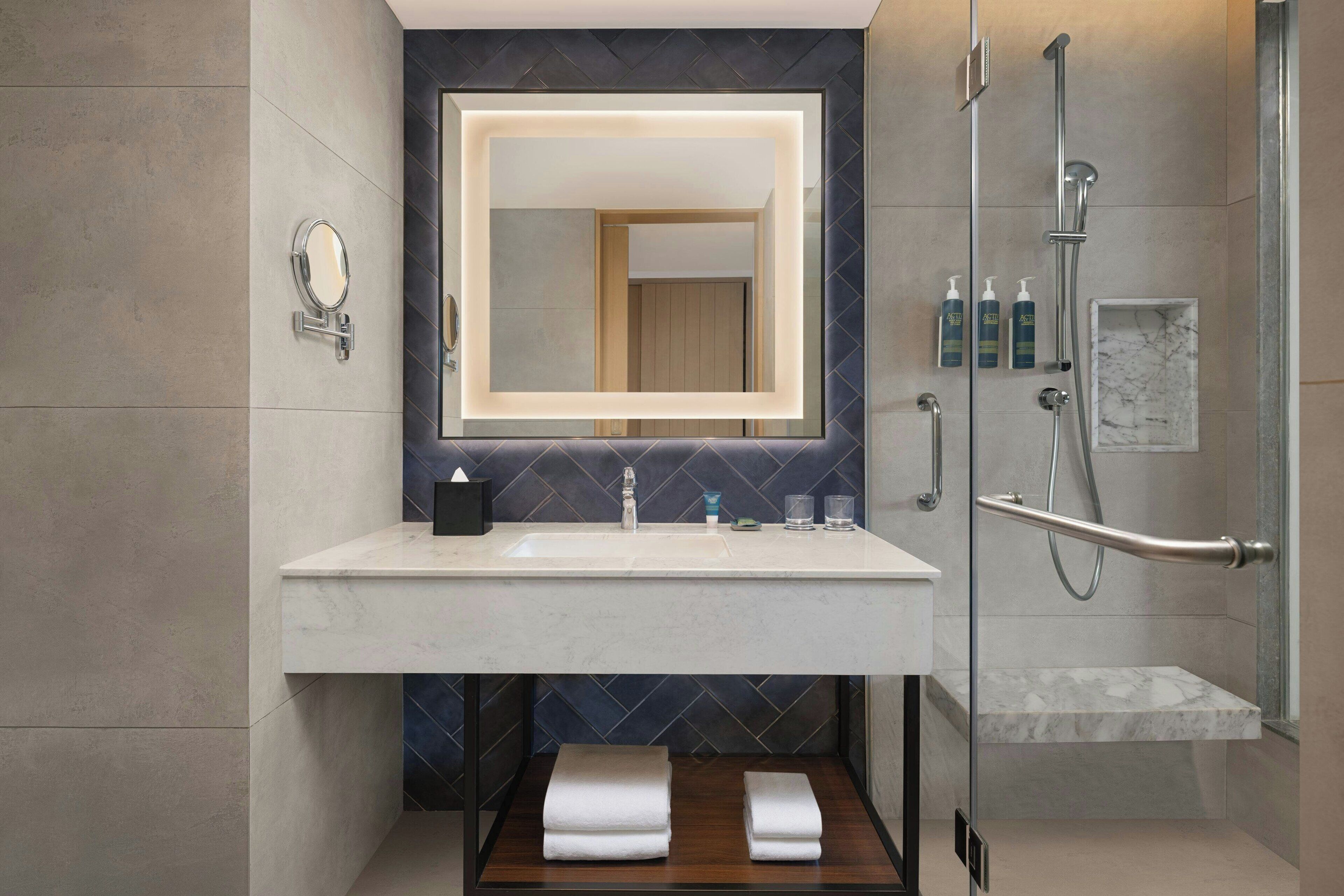 A modern bathroom with a large mirror, a sink, and a shower area.
