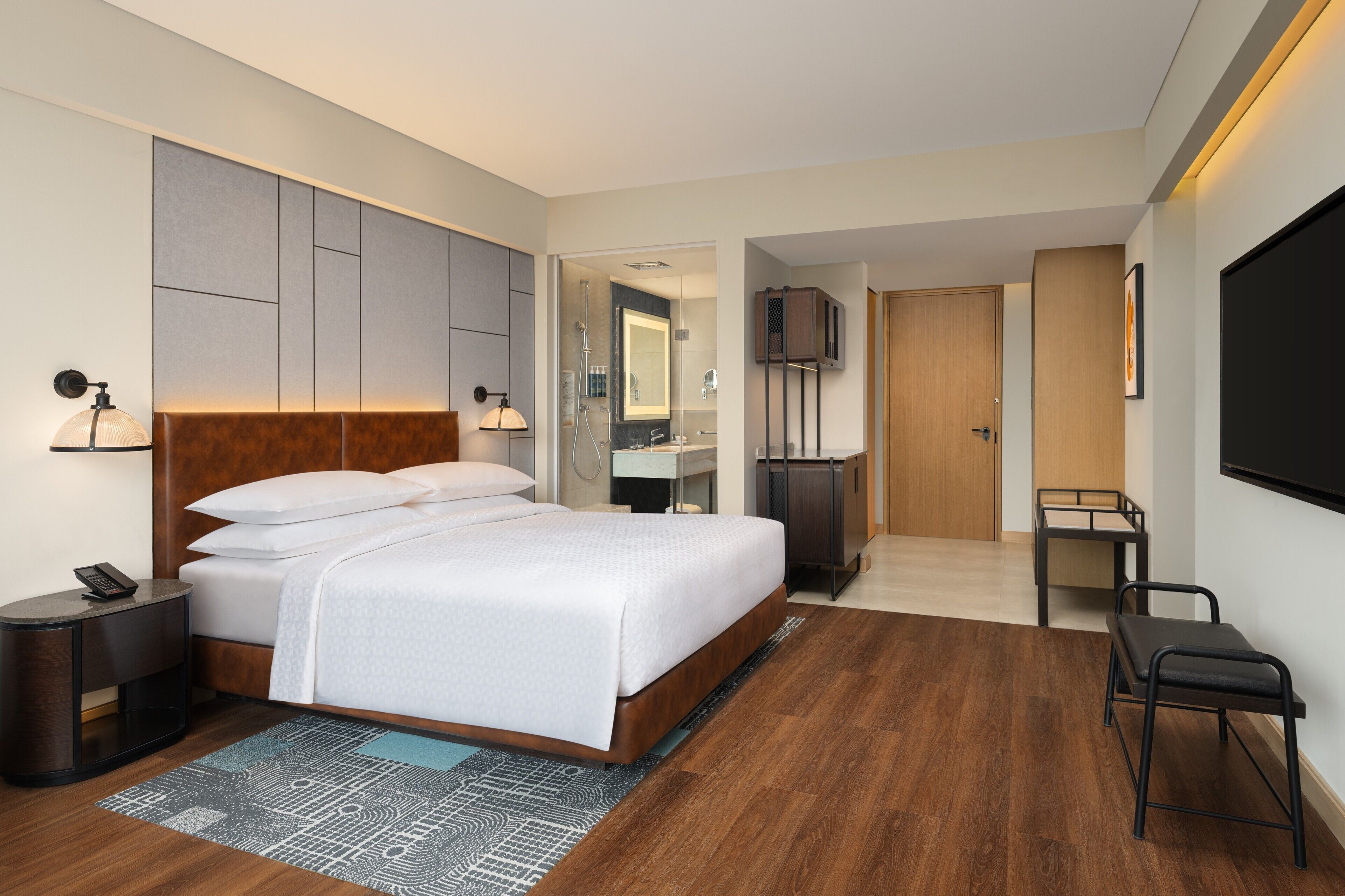 A modern hotel room with a large bed, bedside tables, a desk, and a TV.
