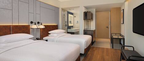 A hotel room with two beds, a desk, a TV, and a bathroom visible through an open door.