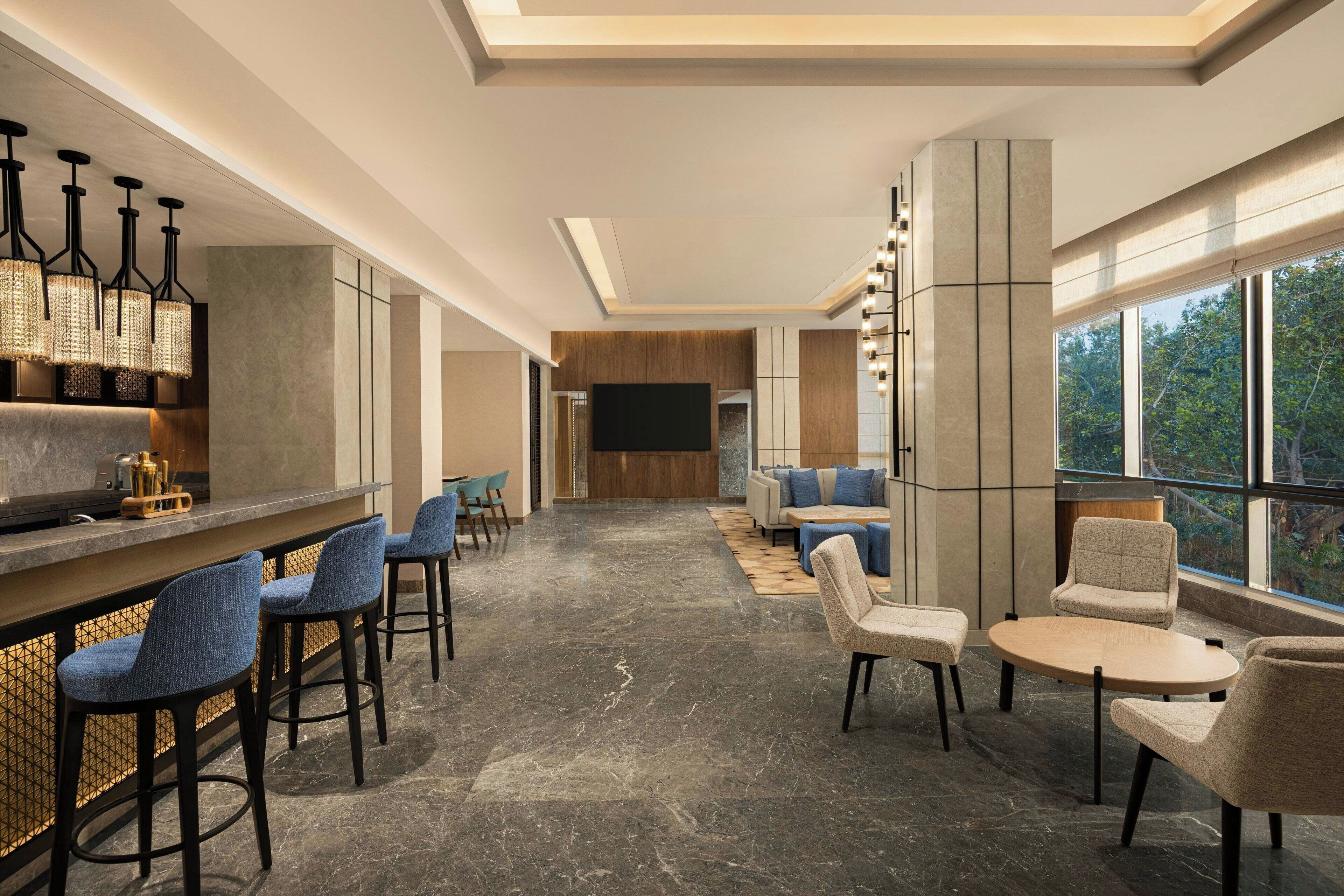 A modern bar area with seating, a television, and large windows offering a view of the outdoors.