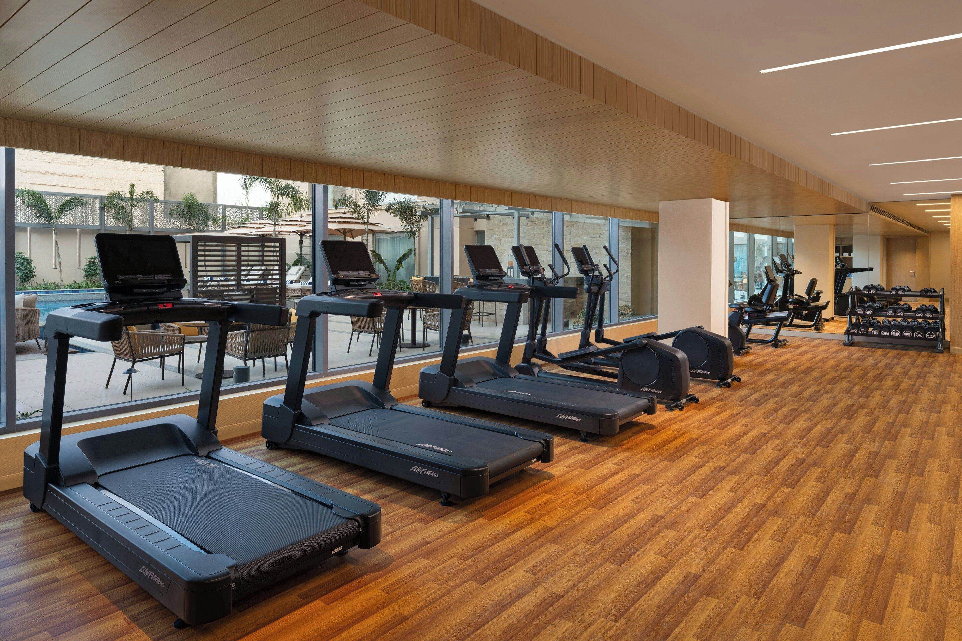 A gym with treadmills, weight machines, and a pool area visible through large windows.