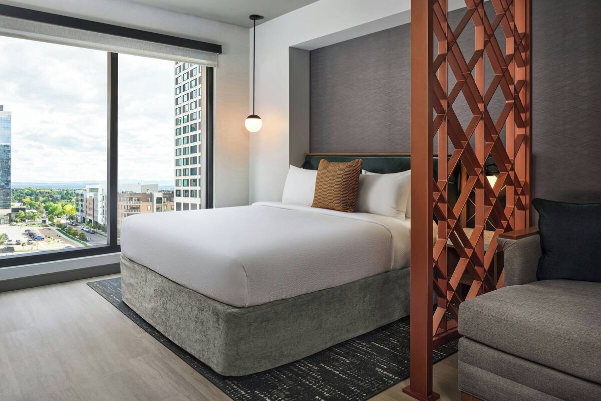 Una habitación de hotel moderna con una cama grande, vista a la ciudad y un separador decorativo de madera.