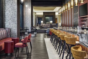 A modern bar area with a long counter, multiple stools, and a seating area with sofas and chairs. - Apiary Hotel Belleview Station Denver (Denver)
