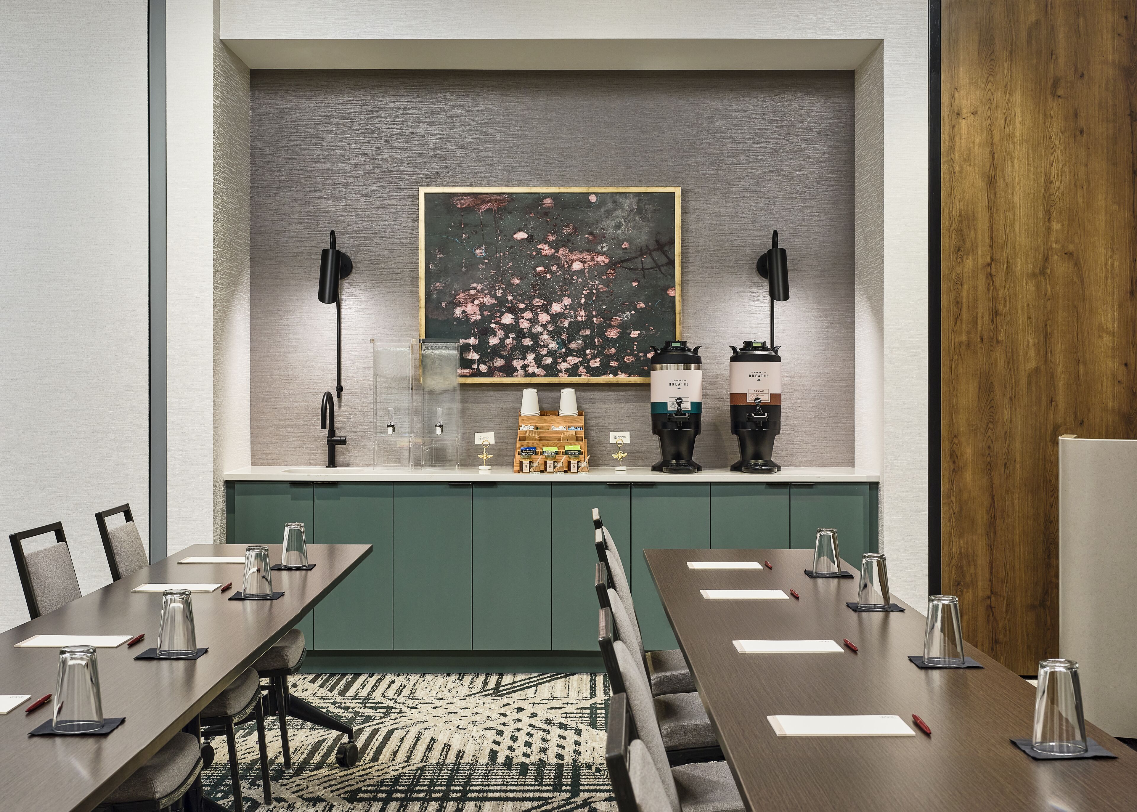 A conference room with a long table, chairs, coffee makers, and a painting on the wall.