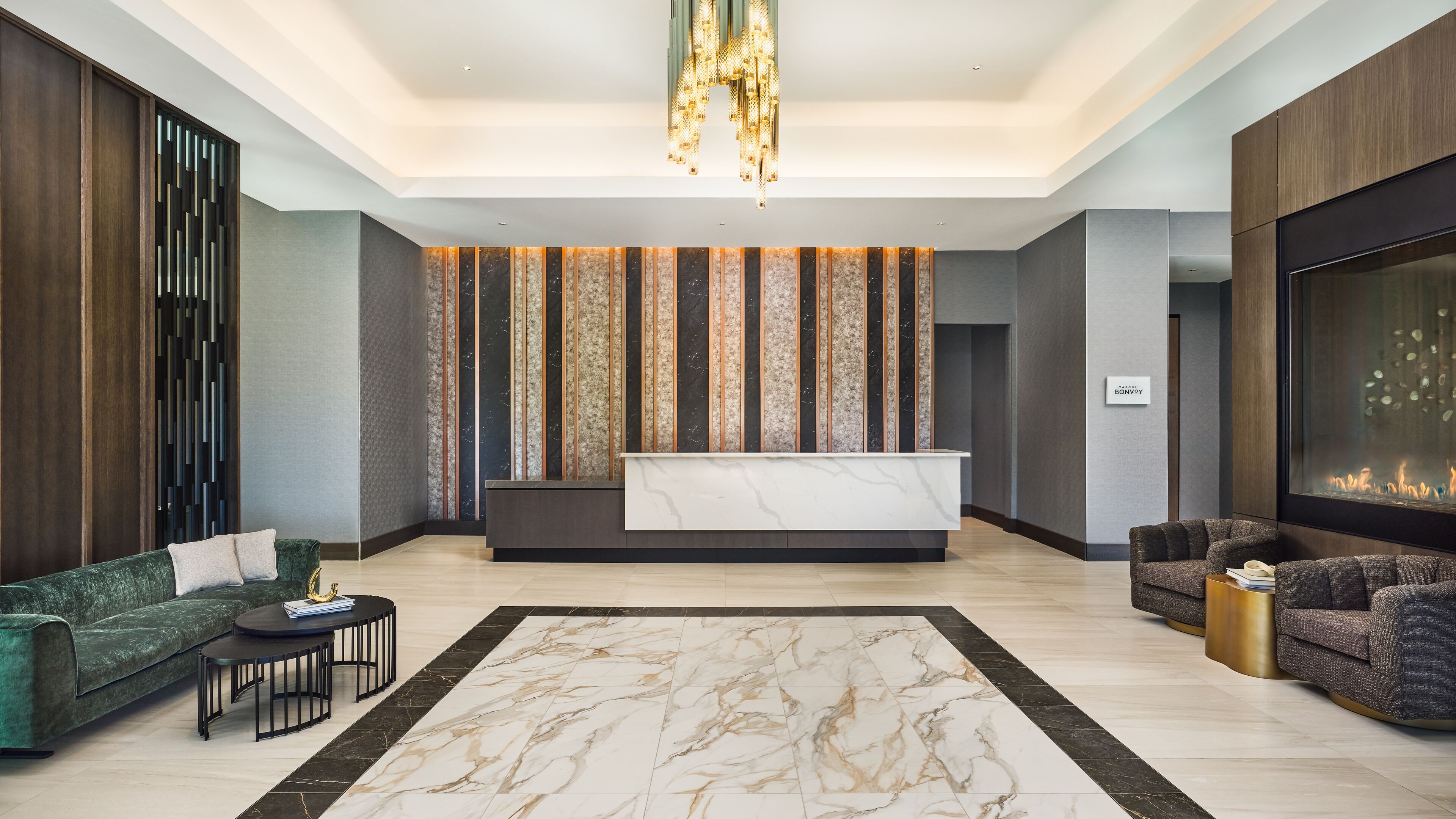 Um lobby moderno com balcão de recepção, sofás, lustre e lareira.