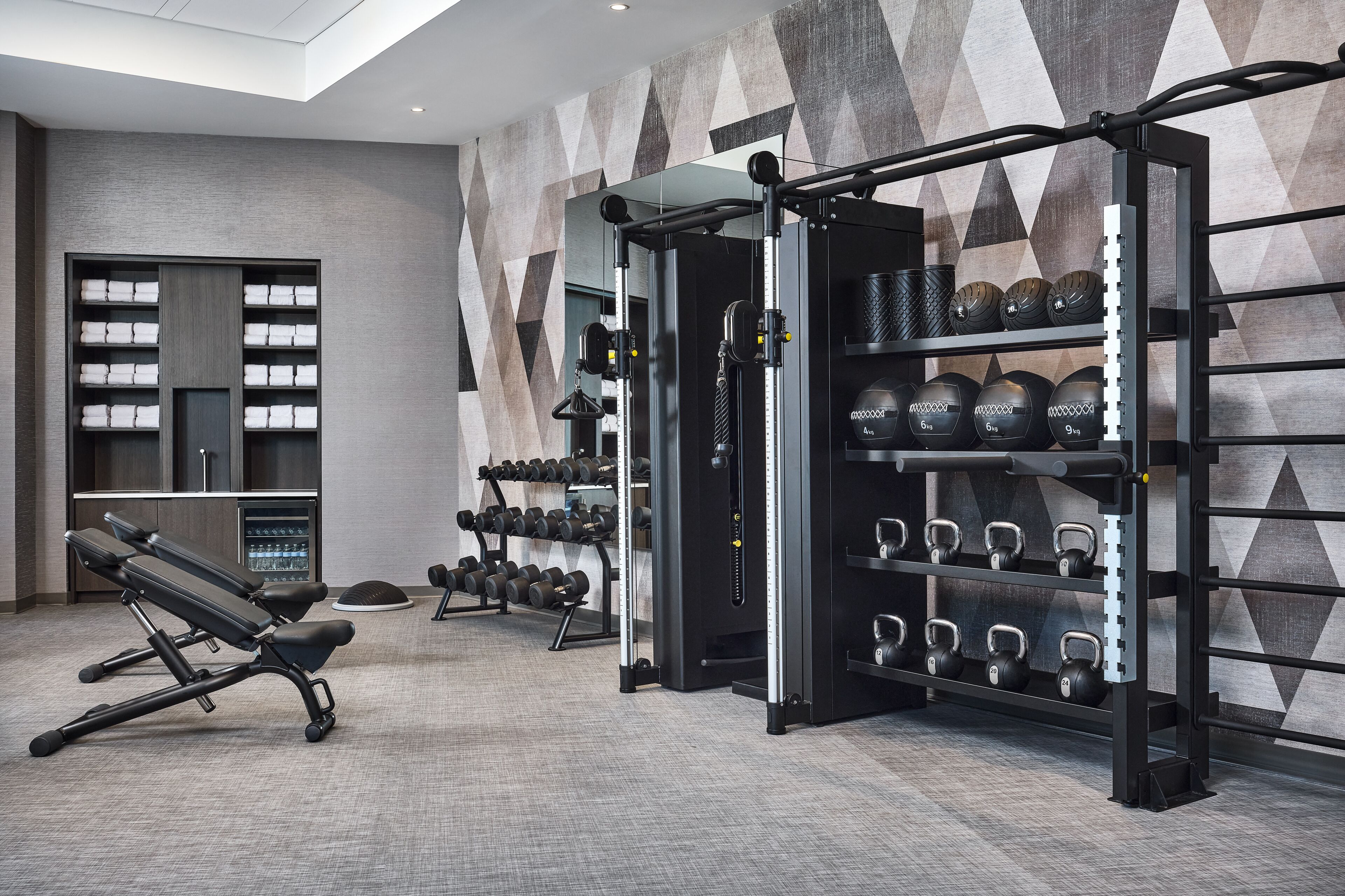 Ein Fitnessraum mit Trainingsgeräten, einem an der Wand befestigten Kettlebell-Ständer und einer Bank.