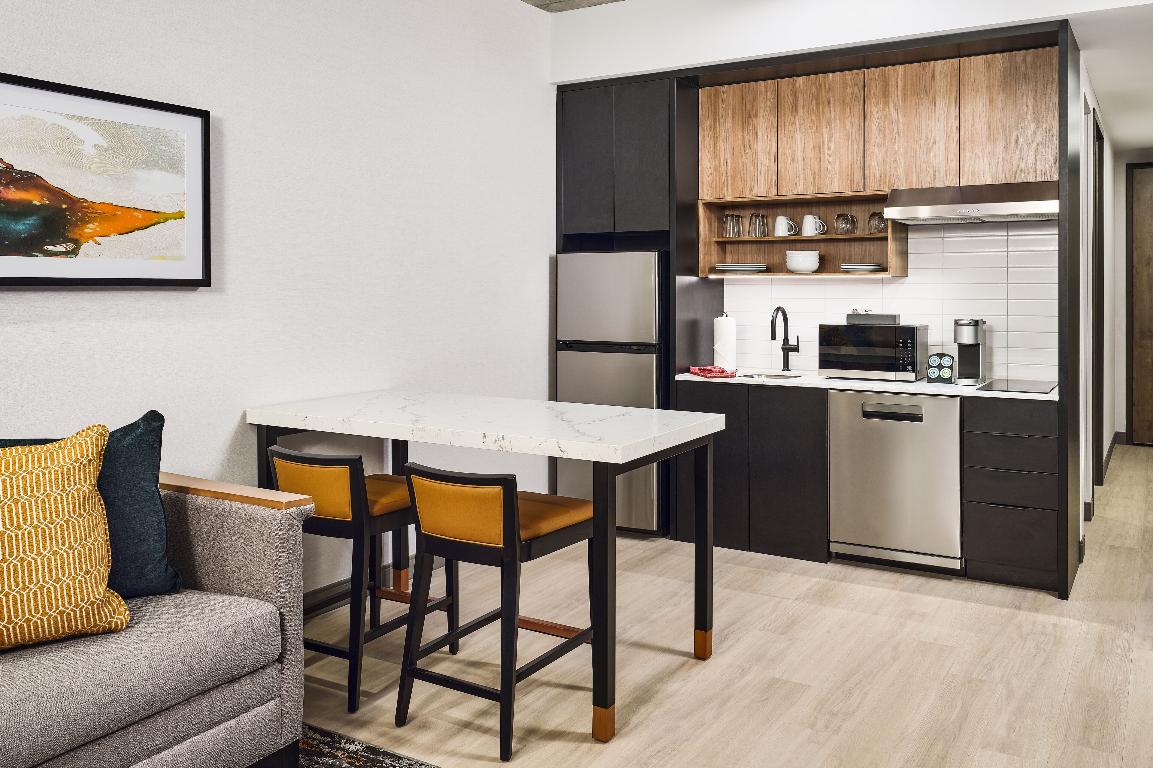 A compact kitchen with a dining area, a sofa, and a framed picture on the wall.