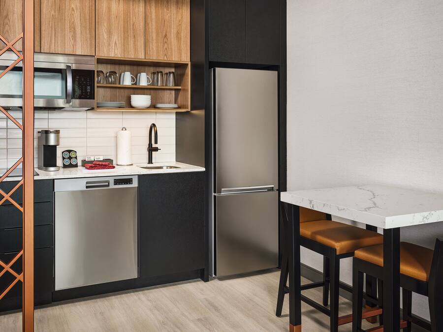 Cozinha moderna com eletrodomésticos de aço inoxidável, máquina de lavar louça, frigorífico e bancada de mármore.