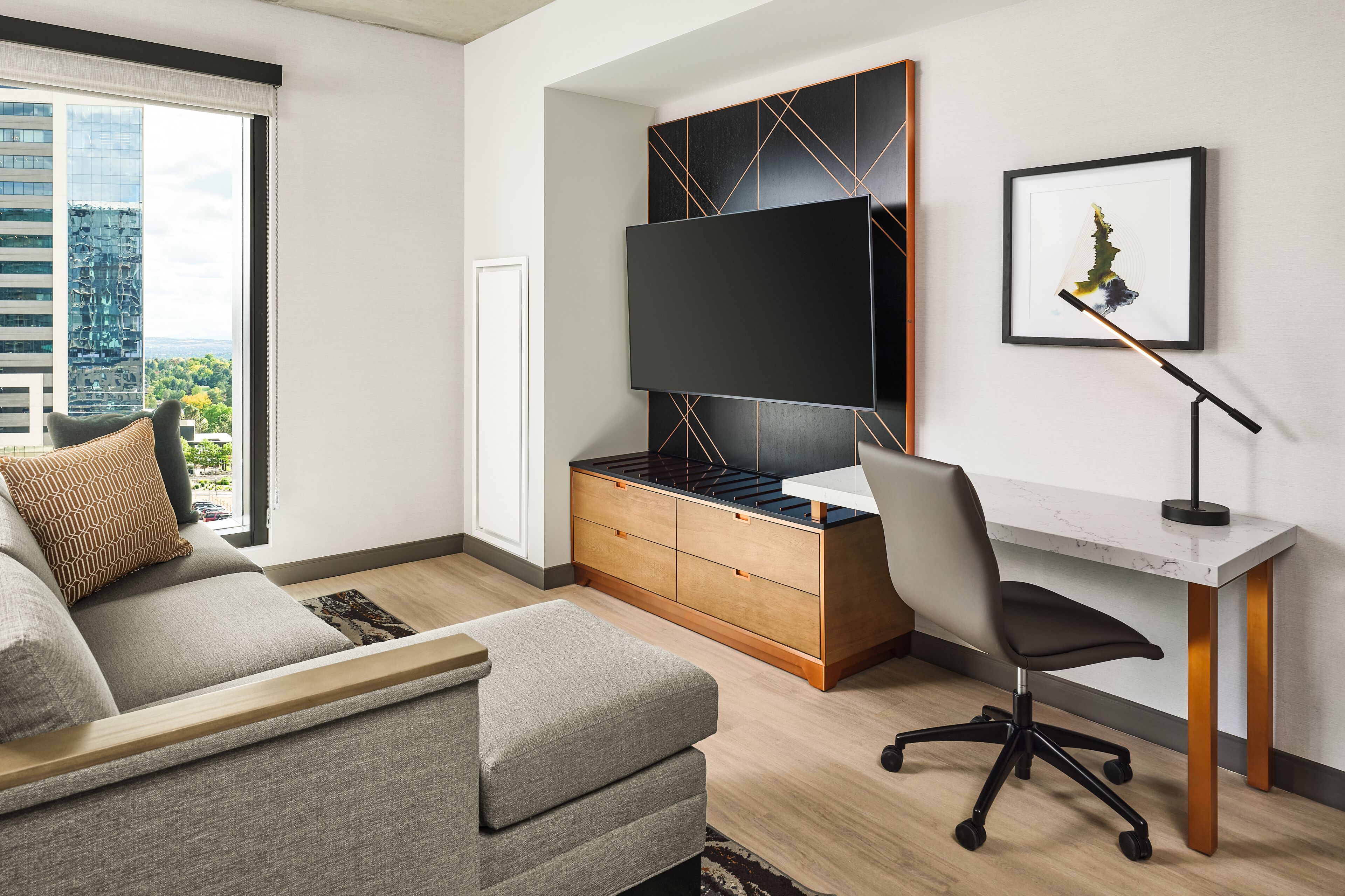 A modern living room with a sofa, a desk, a chair, a TV, and a framed picture on the wall.