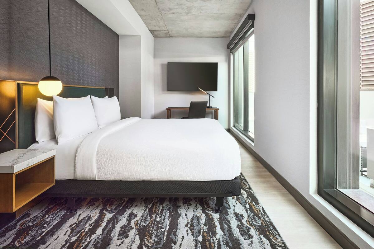 Una habitación de hotel moderna con una cama grande, un escritorio, un televisor de pantalla plana y un ventanal amplio.