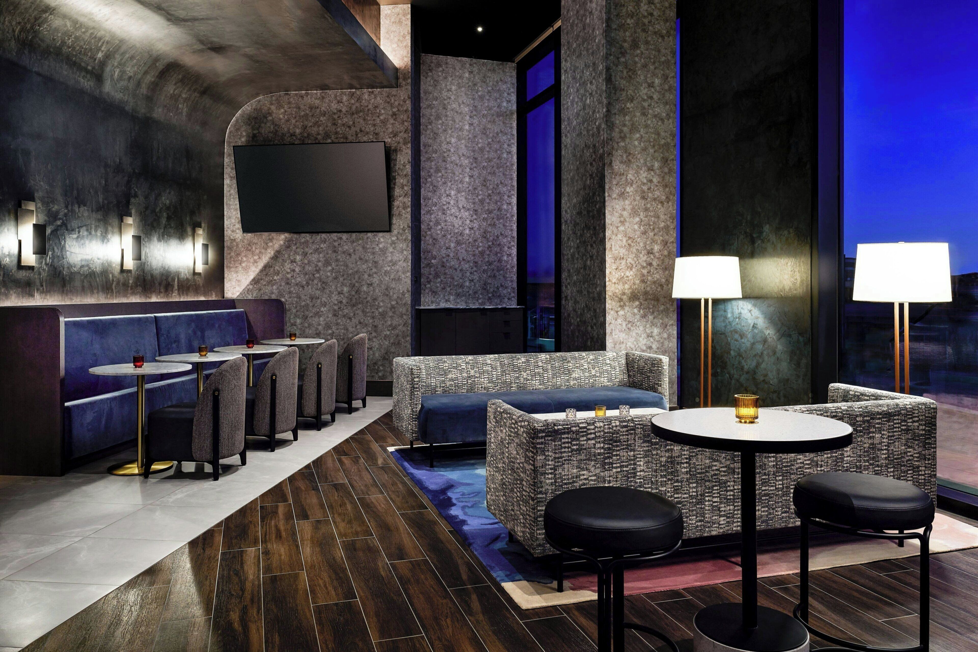 Un espace de détente moderne, doté de canapés, de tables rondes et de tabourets de bar, avec un grand écran de télévision et une vue par la fenêtre.