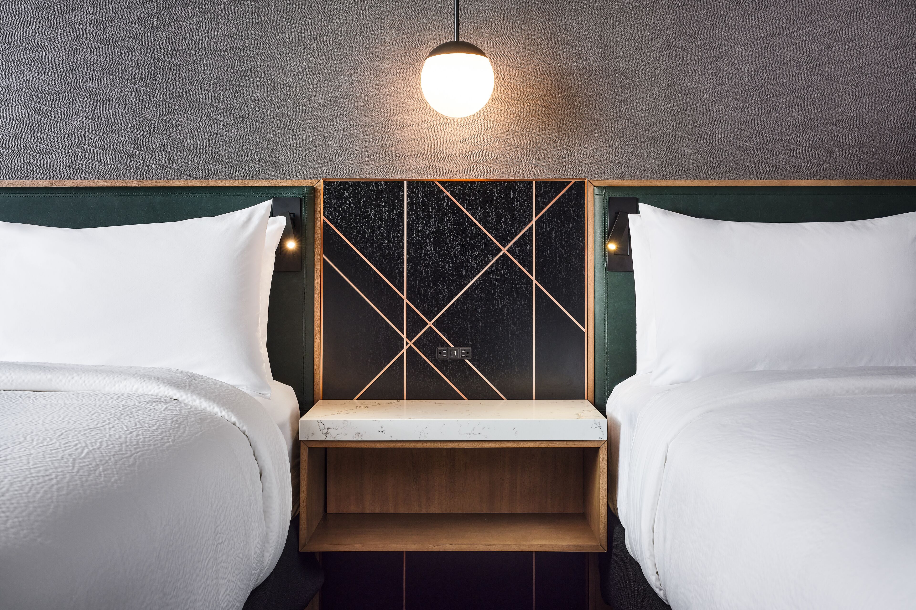 A room with two beds, a wooden bench, a wall-mounted light fixture, and a textured ceiling.