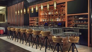 Una zona de bar con taburetes, una barra y estantes con botellas.