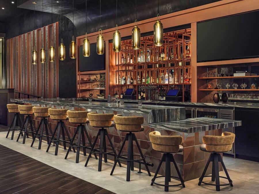 Una zona de bar con taburetes, una barra y estantes con botellas.