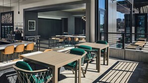 Un espacio moderno al aire libre para comer, con mesas, sillas y una barra, y vistas a la ciudad.