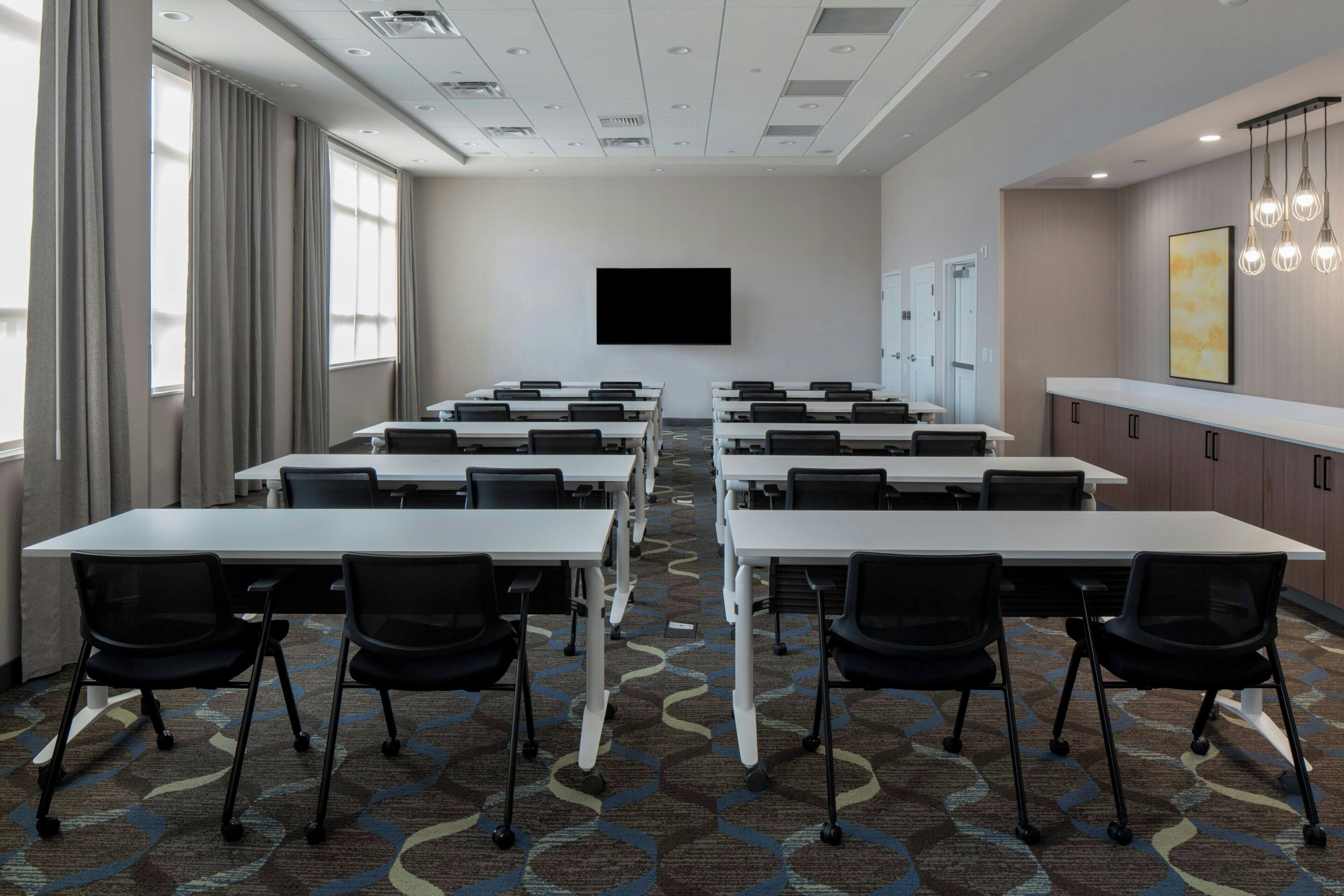 A conference room with multiple tables and chairs, a flat-screen TV, and a patterned carpet.