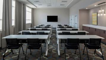 A conference room with multiple tables and chairs, a flat-screen TV, and a patterned carpet.