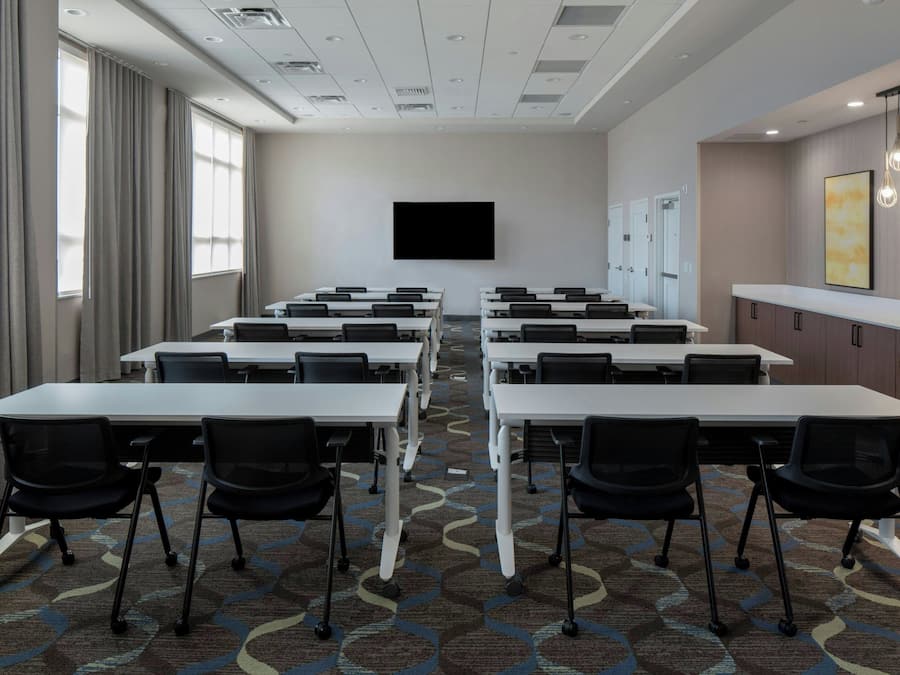 A conference room with multiple tables and chairs, a flat-screen TV, and a patterned carpet.