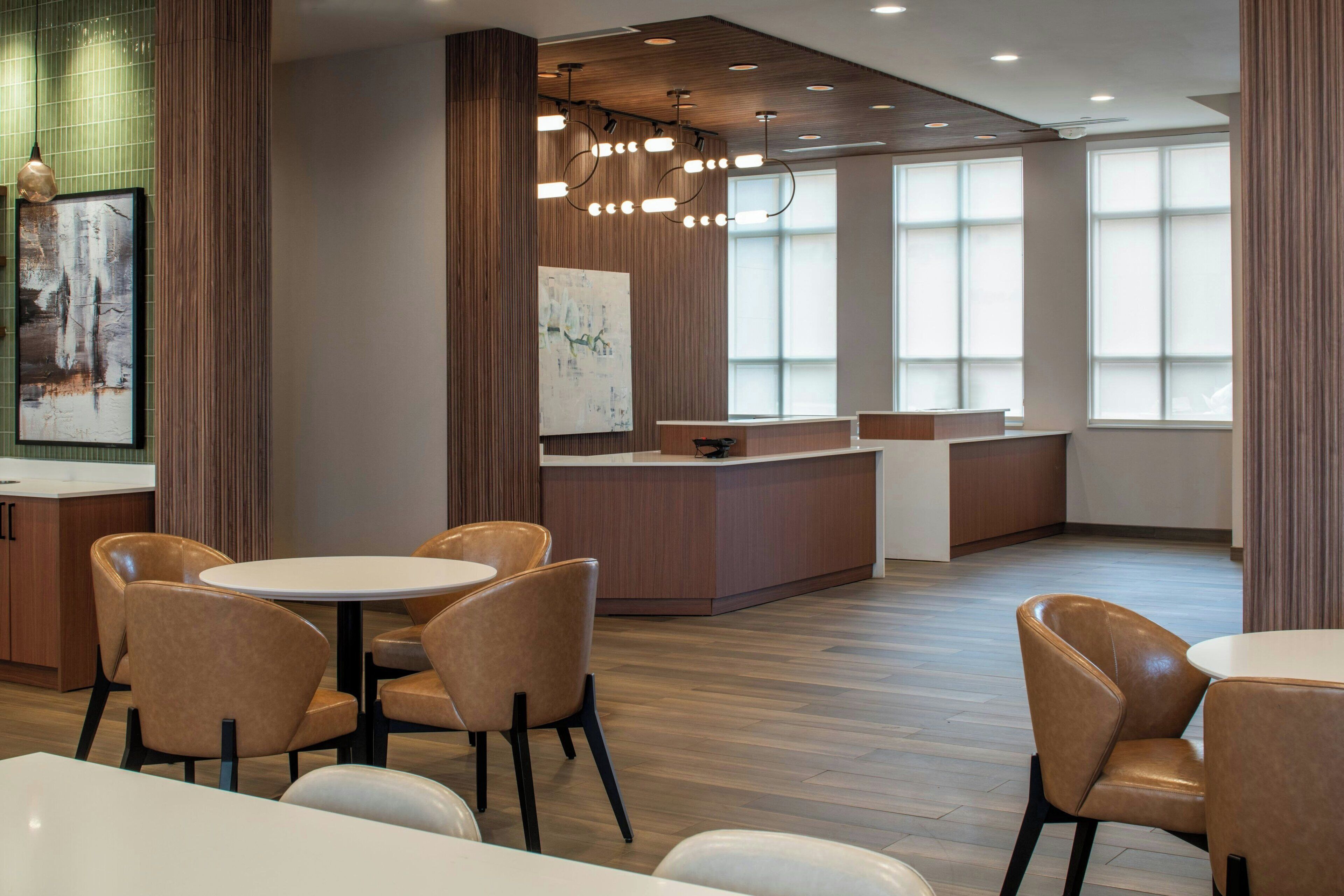 A modern restaurant with round tables and cushioned chairs, wooden flooring, and large windows.