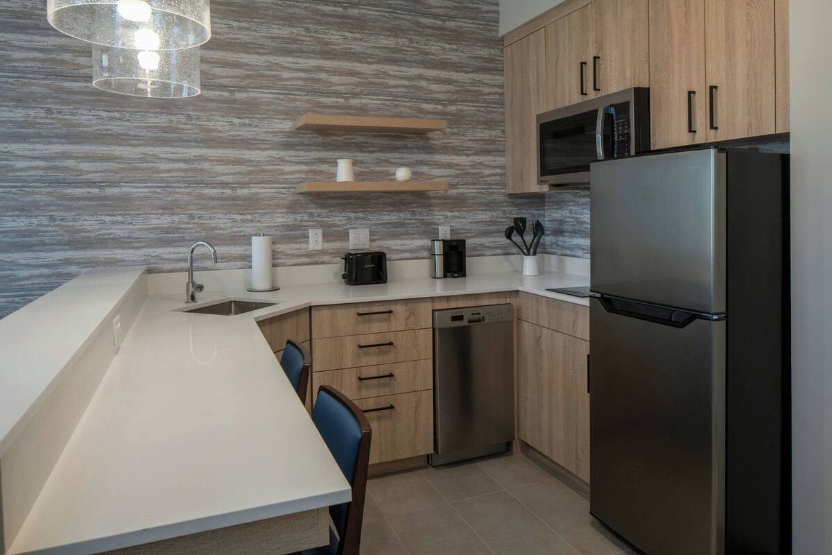 Una cocina moderna con refrigerador de acero inoxidable, armarios de madera, lavavajillas y microondas.